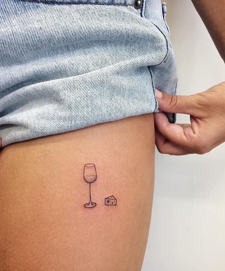 3. Ein Käseblock und ein Glas Wein als Tattoo auf dem Oberschenkel