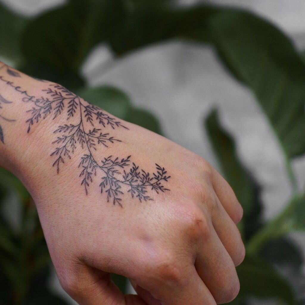 Ein zartes und zierliches Farn-Tattoo auf der Hand