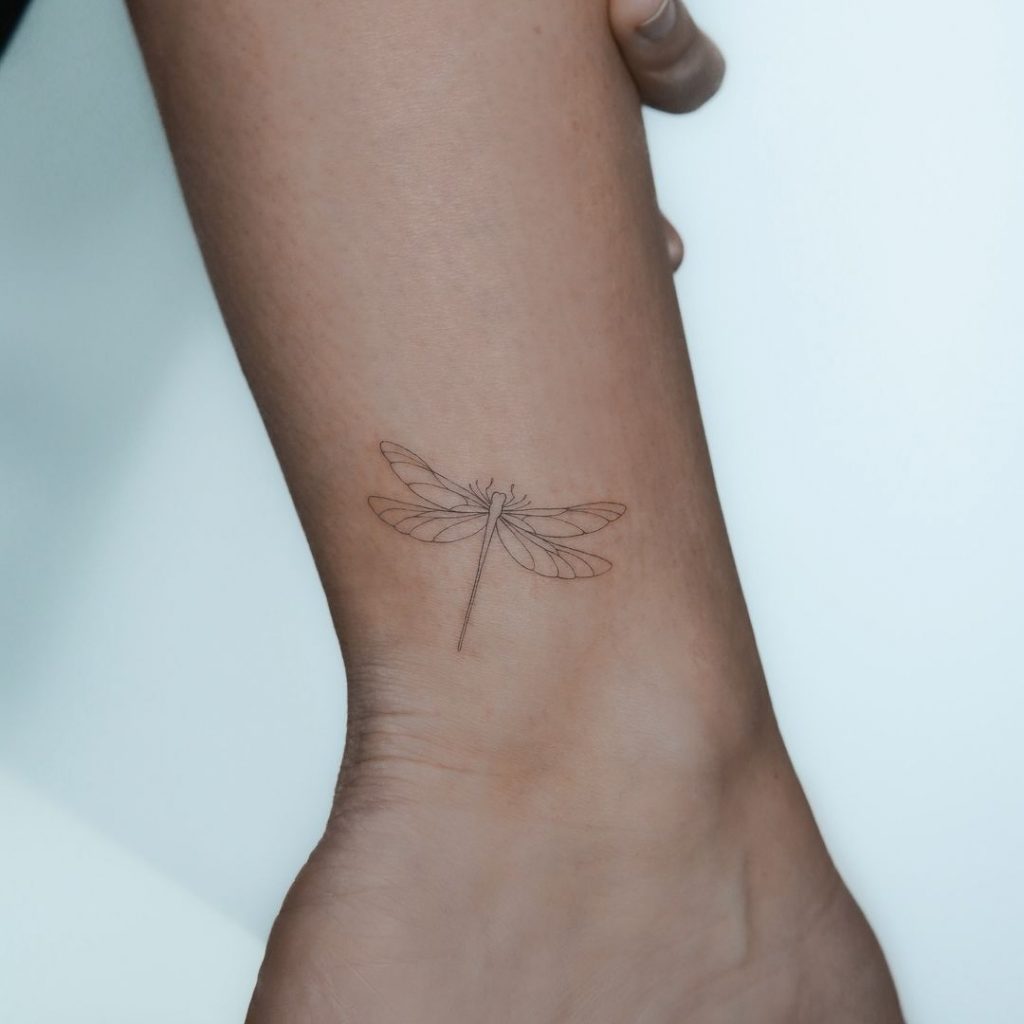 Eine Tätowierung einer zarten Libelle auf dem Knöchel