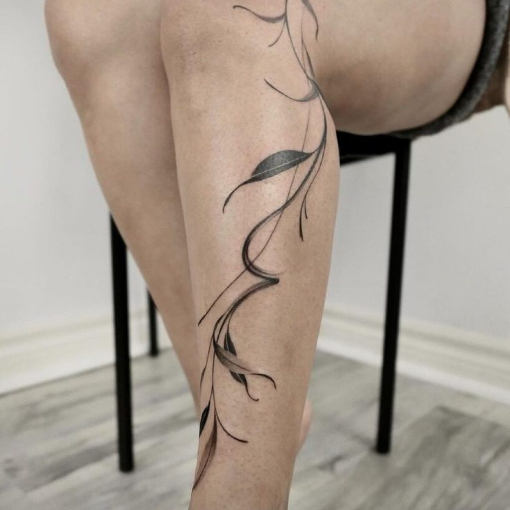 Ein pinselstrichartiges Schienbein-Tattoo aus Blättern und Ranken