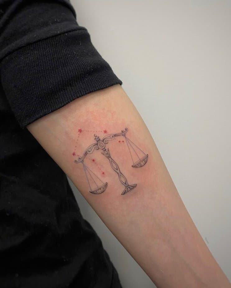 17. Ein Tattoo der Waage mit roter und schwarzer Tinte auf dem Unterarm